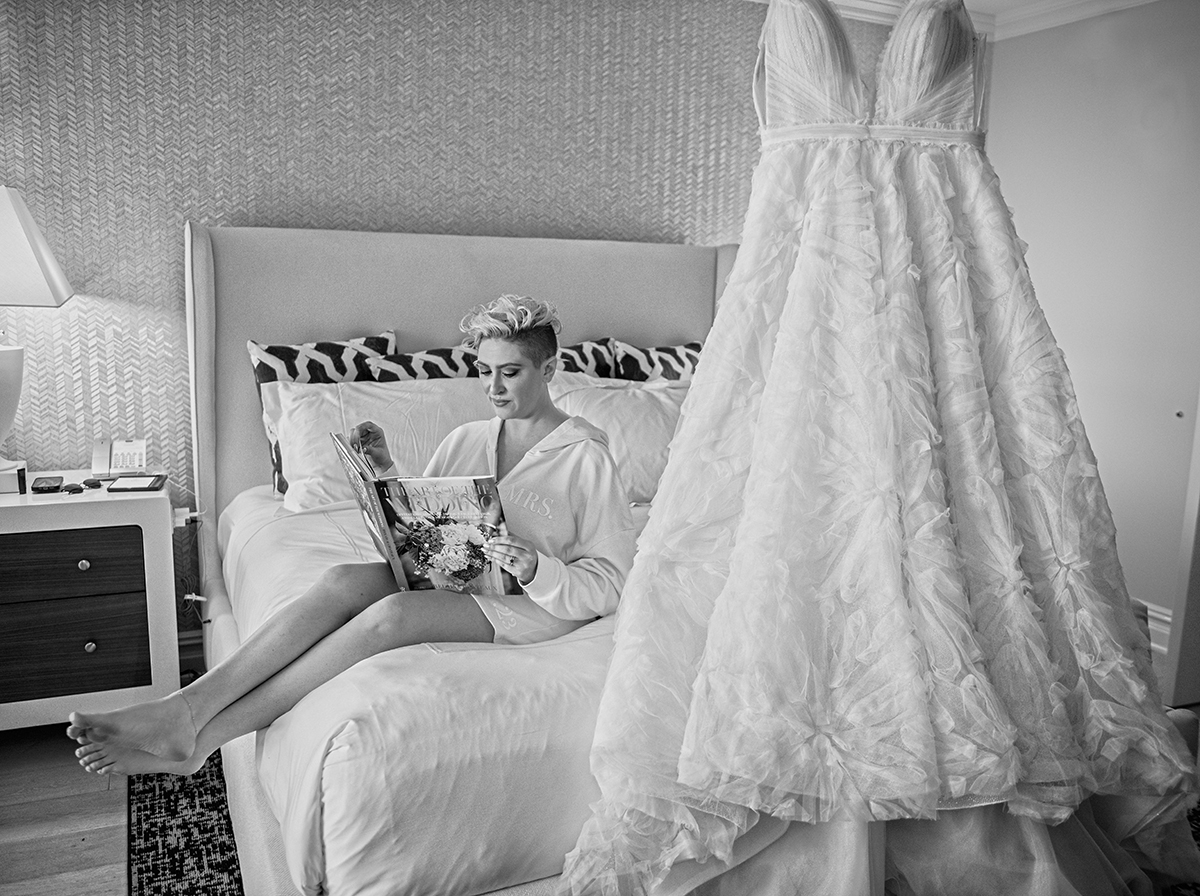 Bride relaxing on the bed in her South Florida bridal suite reading a magazine beside her hanging wedding gown before getting dressed.