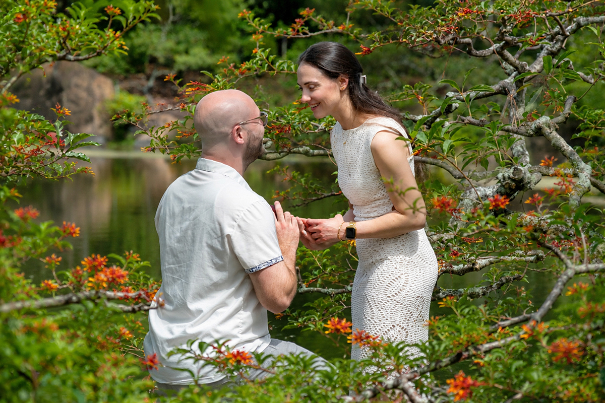 Nathan proposes to Alyssa at the Morikami Museum and Japanese Gardens in Delray Beach, Florida, during a surprise marriage proposal photographed through flowering trees.