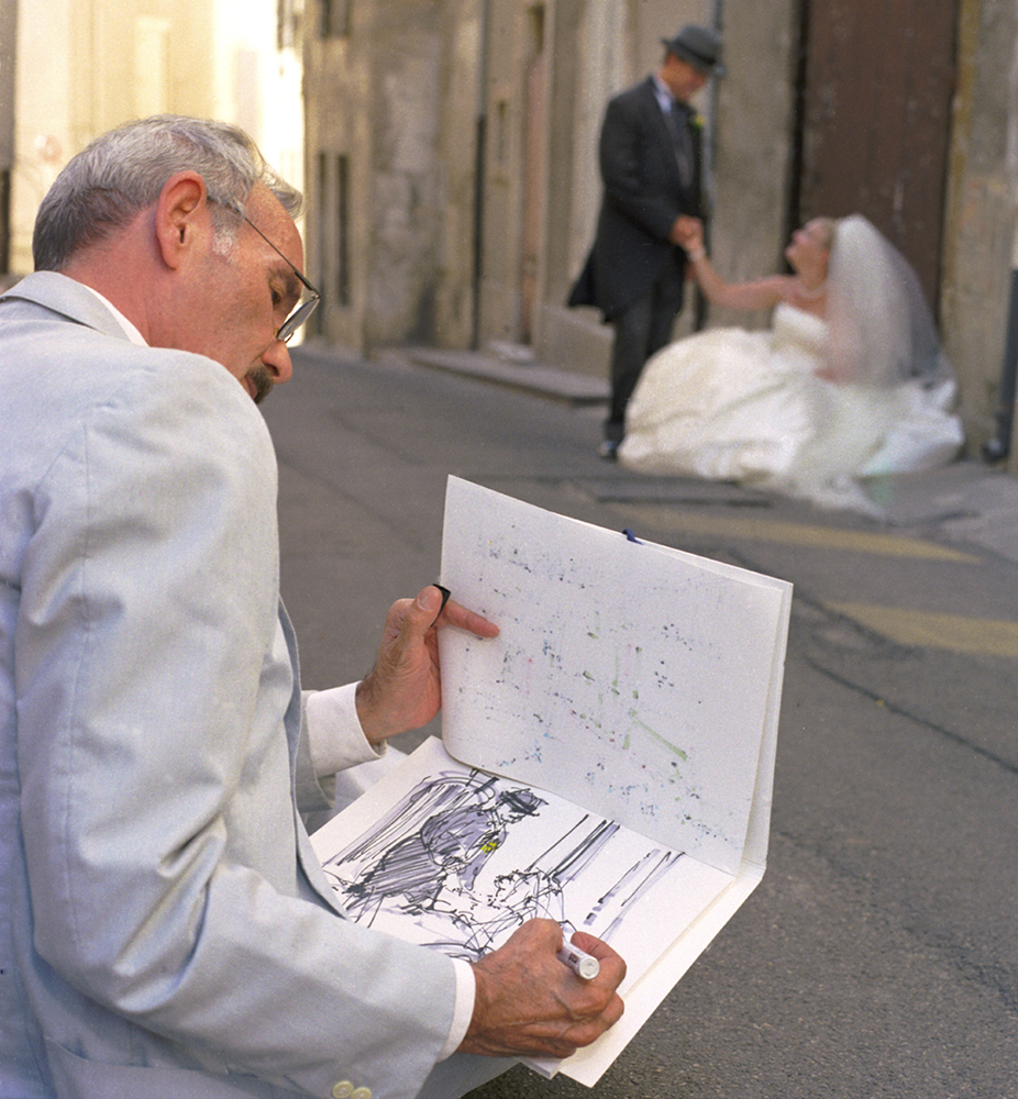 A South Florida wedding photographer captures a romantic moment in Avignon, France, as an artist sketches the bride and groom during their wedding photo session.