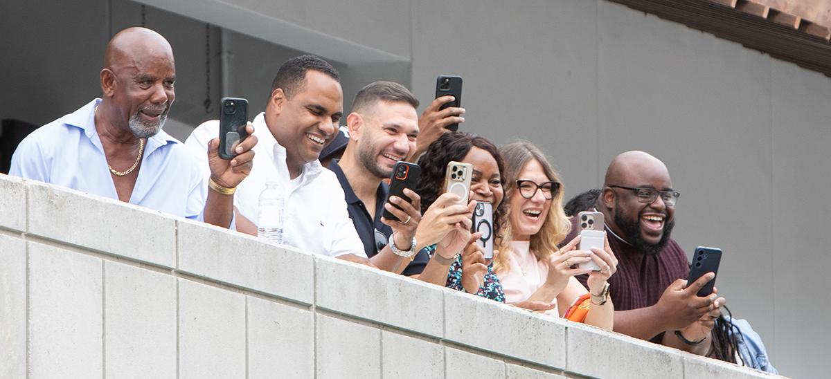 Excited family and friends smiling and holding up phones from an upper terrace at Morikami Museum in Delray Beach during a surprise marriage proposal