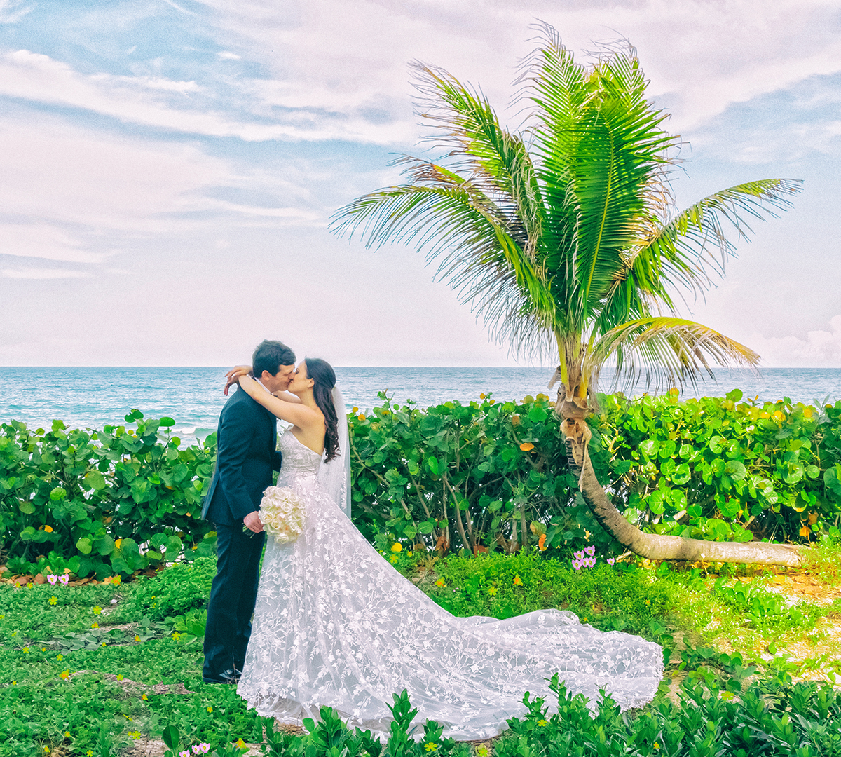 Bride and groom embrace by a palm tree overlooking the Atlantic Ocean at The Hillsboro Club in Fort Lauderdale, captured by South Florida wedding photographer Jeff Kolodny.