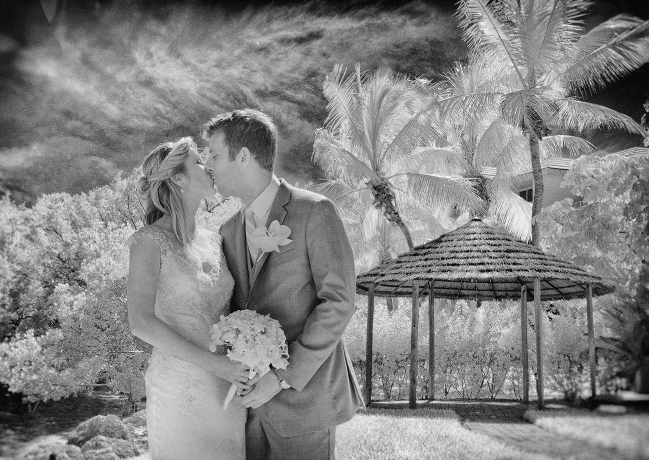 Bride and groom share a kiss under palm trees in the Florida Keys, captured in artistic black-and-white infrared photography by South Florida wedding photographer Jeff Kolodny.