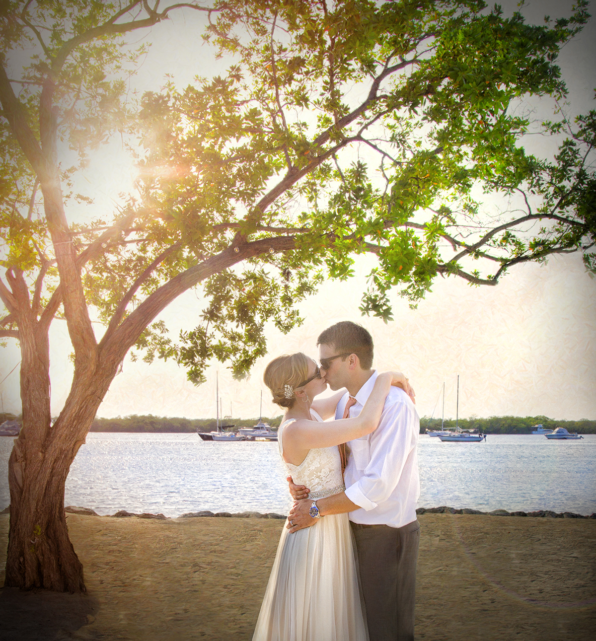Bride and groom kissing under a leafy tree at sunset along the beach in the Florida Keys, captured by South Florida Wedding Photographer Jeff Kolodny during golden hour.