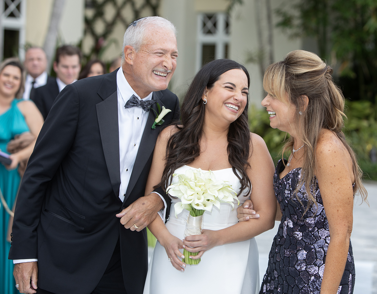 Bride walking down the aisle at Woodfield Country Club in Boca Raton, laughing with her parents during a joyful South Florida wedding ceremony.