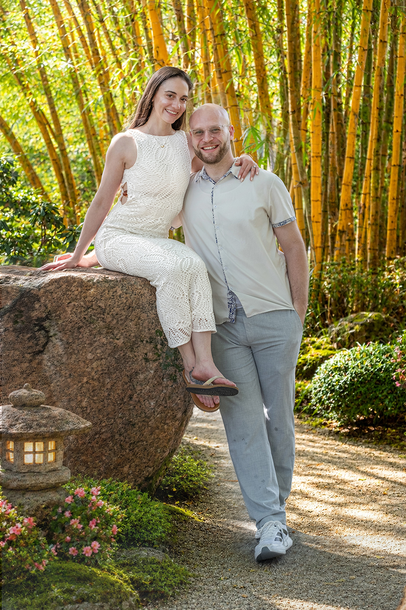 Nathan and Alyssa pose on a large rock surrounded by bamboo at the Morikami Museum and Japanese Gardens after their surprise marriage proposal in Delray Beach, Florida.