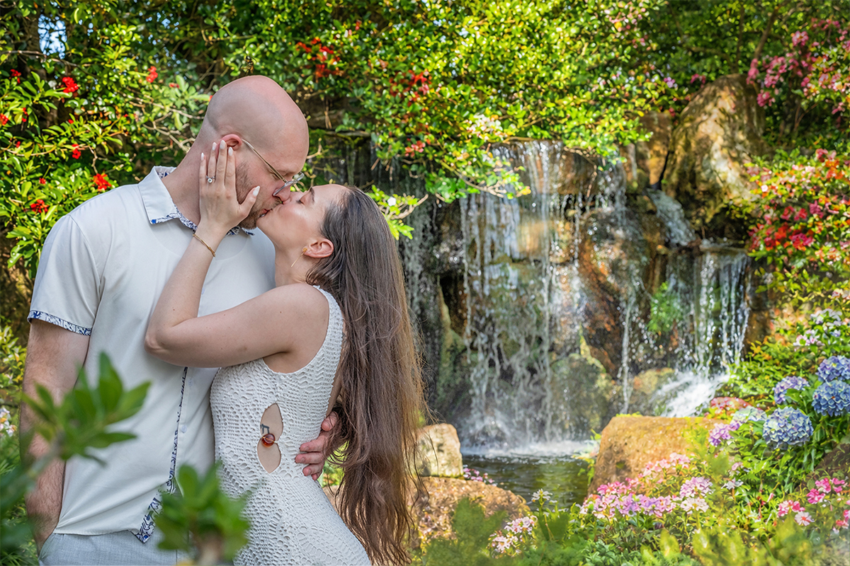 Nathan and Alyssa share a kiss in front of a waterfall at the Morikami Museum and Japanese Gardens after their surprise marriage proposal in Delray Beach, Florida.