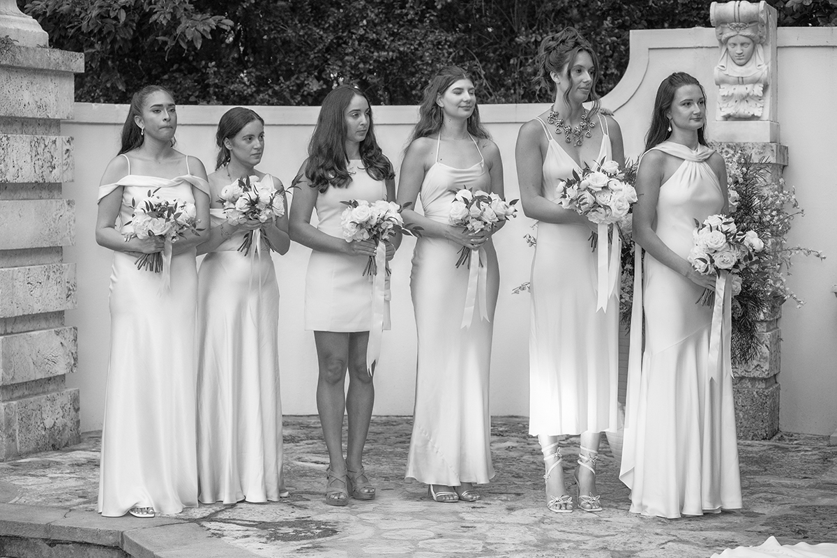 Black and white photo of bridesmaids lined up holding bouquets during Bonnet House wedding ceremony in Fort Lauderdale watching the bride get married.