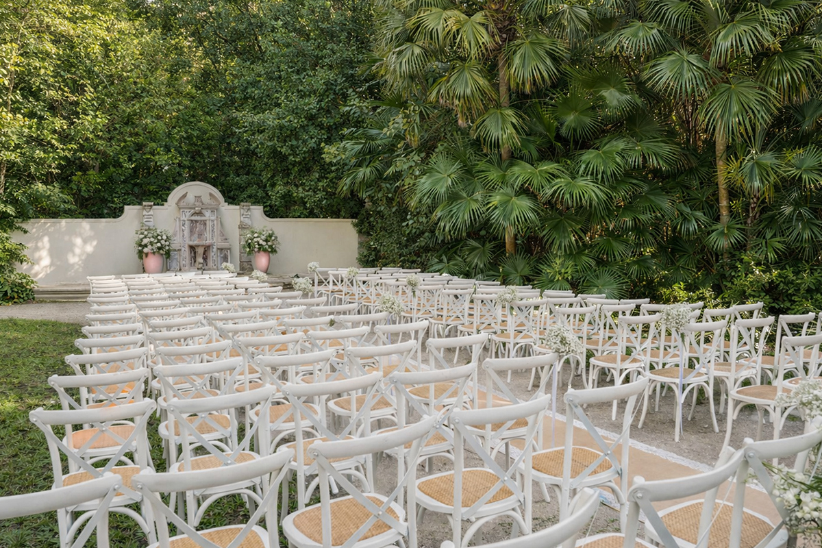 Outdoor wedding ceremony setup at Bonnet House in Fort Lauderdale with white cross-back chairs and lush tropical greenery