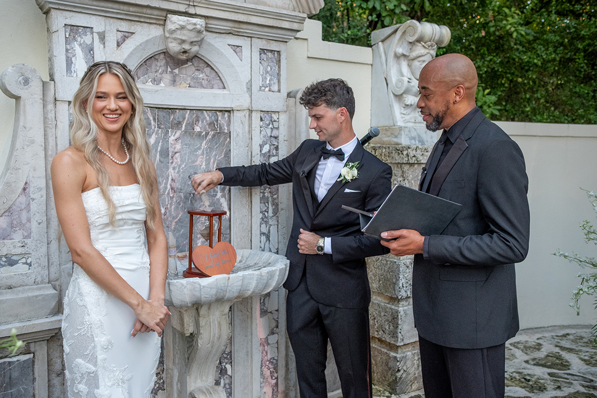 Bride and groom performing sand ceremony at Bonnet House wedding in Fort Lauderdale with historic fountain backdrop and officiant reading vows.