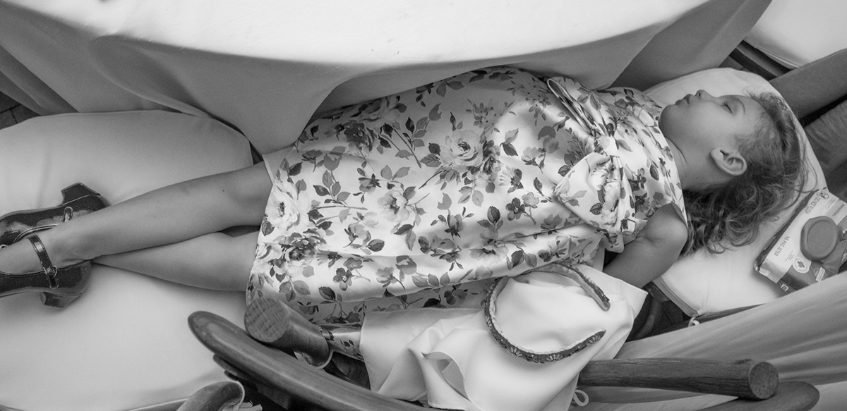 Young girl asleep on makeshift chair bed during a wedding reception at The Bonnet House in Fort Lauderdale while the celebration continues around her.