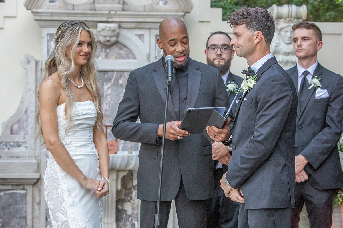 Bride and groom exchanging vows during Bonnet House wedding ceremony in Fort Lauderdale with officiant and groomsmen visible in elegant garden setting.