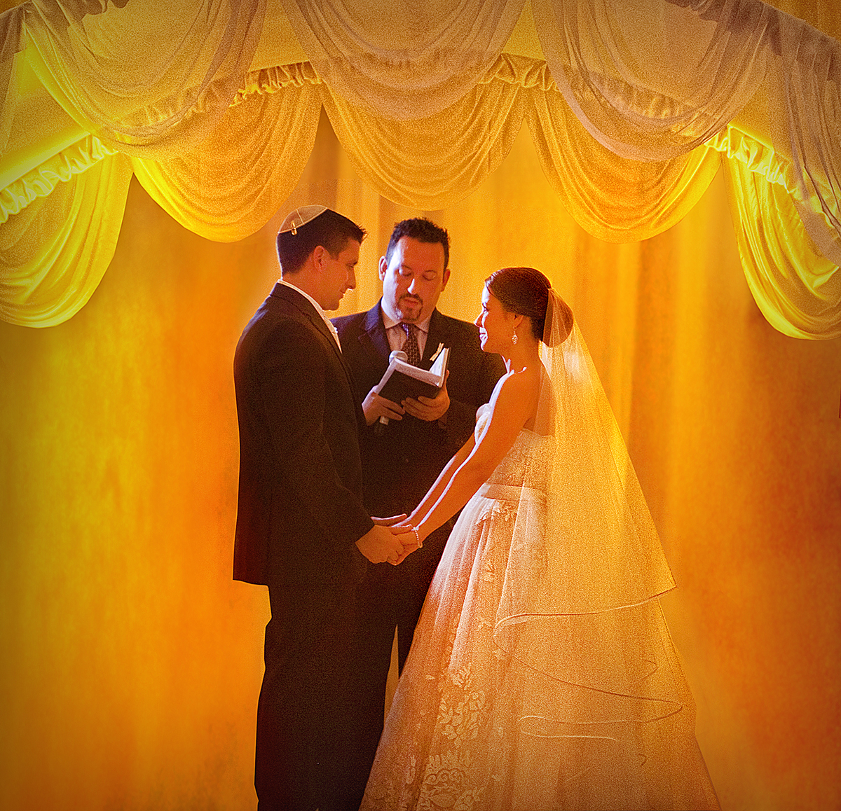 Bride and groom holding hands under a chuppah during a Jewish wedding ceremony at The Ritz-Carlton South Beach, illuminated by warm golden lighting.