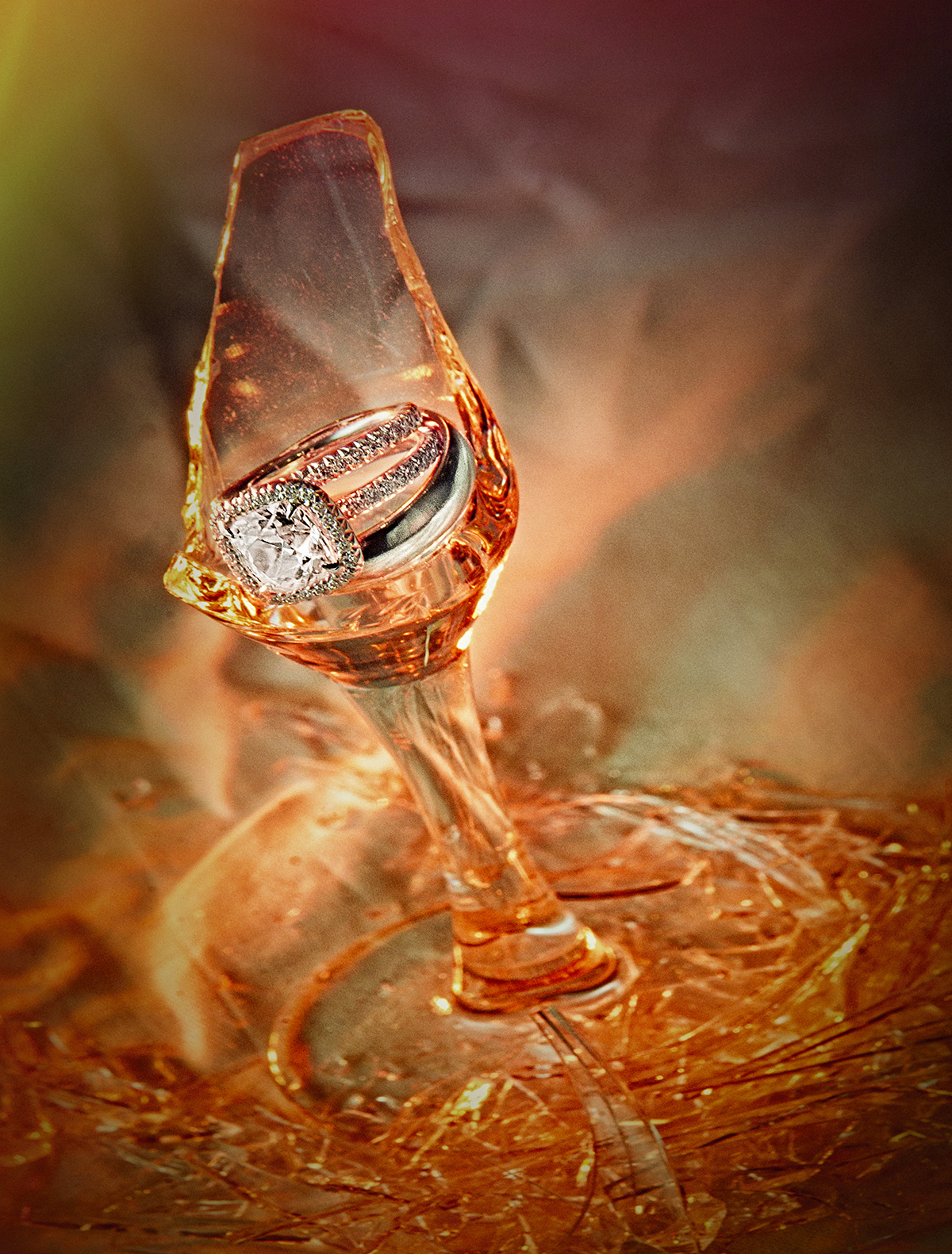 Wedding rings inside an upside-down glass illuminated with warm orange light, symbolizing the Jewish tradition of breaking the glass.