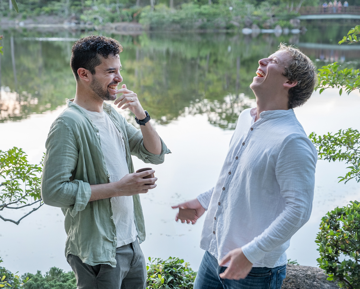 LGBTQ+ proposal photographer at Morikami Museum capturing Steve and Sam laughing together beside the lake after their surprise engagement in Delray Beach, Florida.