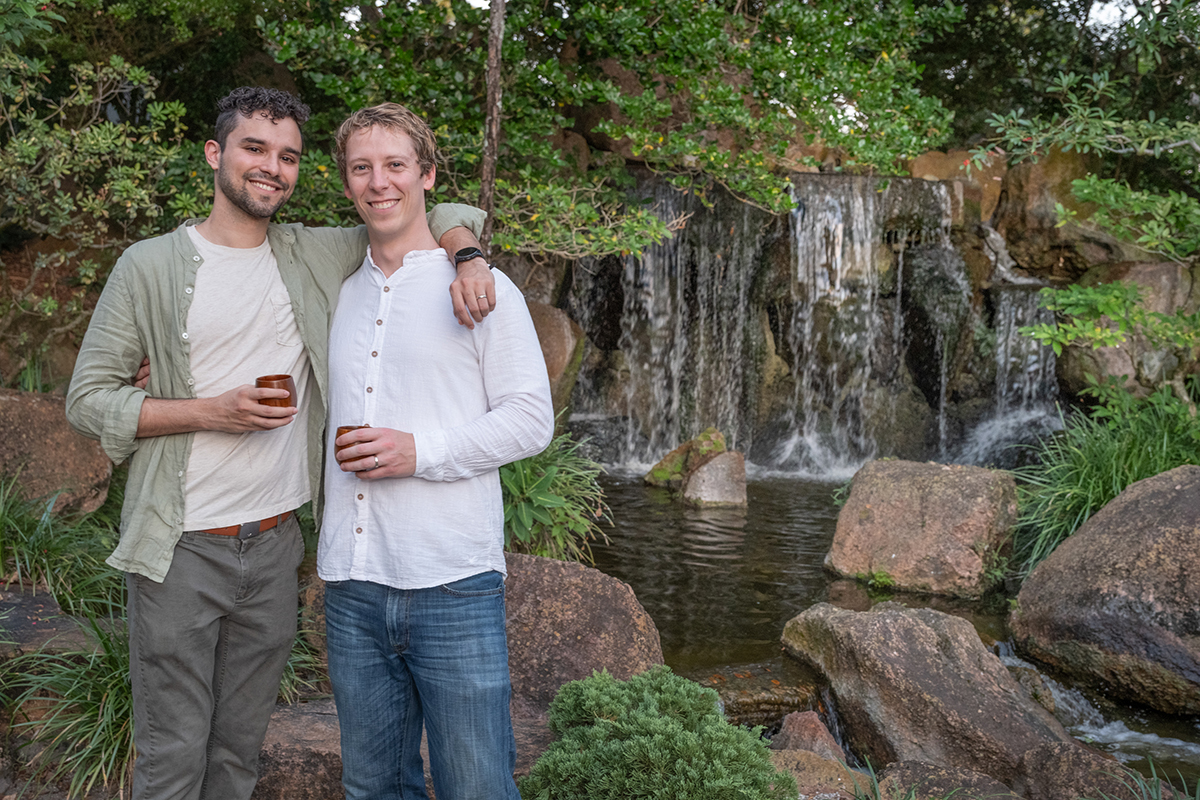 LGBTQ+ proposal photographer at Morikami Museum capturing Steve and Sam posing in front of the waterfall during their surprise engagement session in Delray Beach, Florida.