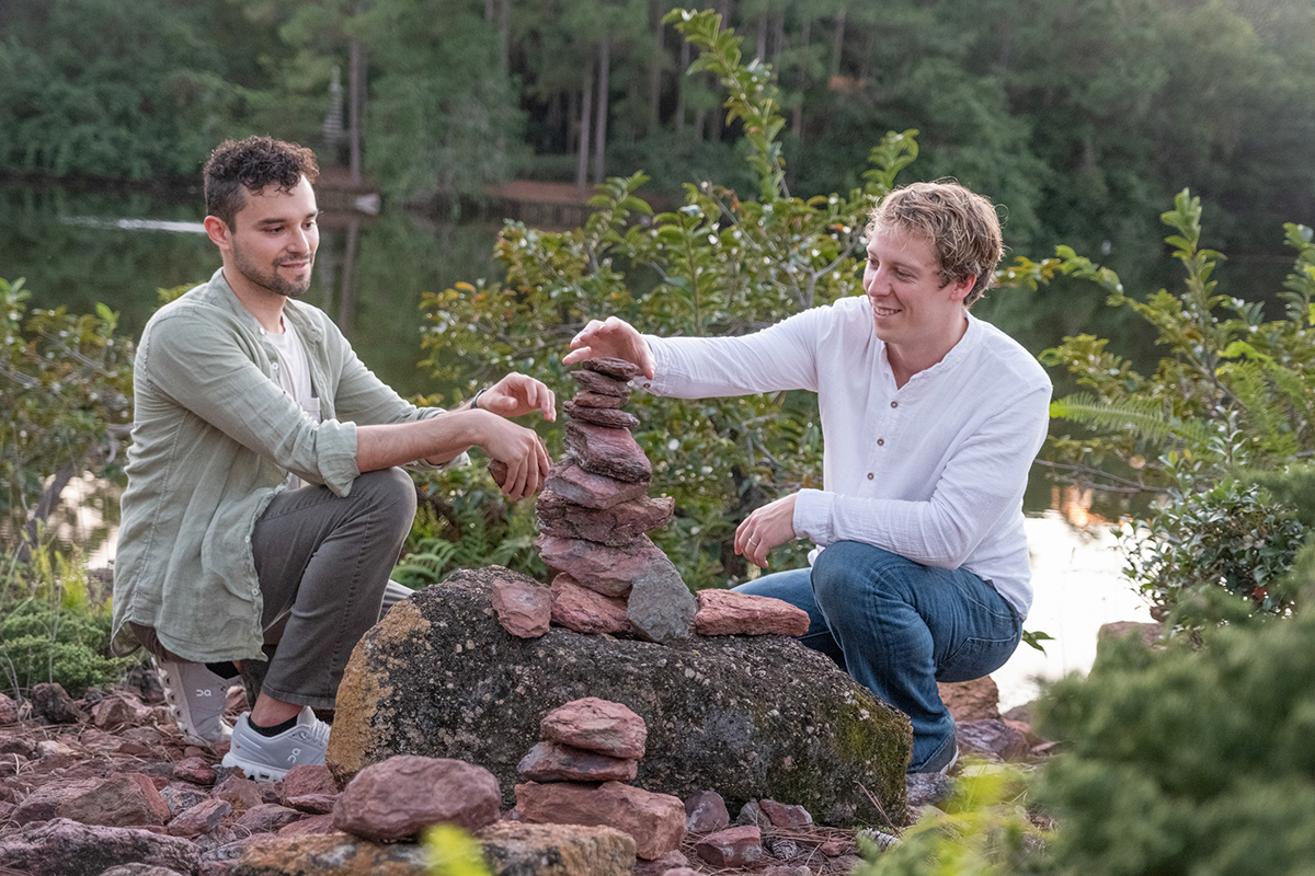 LGBTQ+ proposal photographer at Morikami Museum capturing Steve and Sam creating a stacked stone sculpture beside the lake at Morikami Gardens in Delray Beach, Florida.
