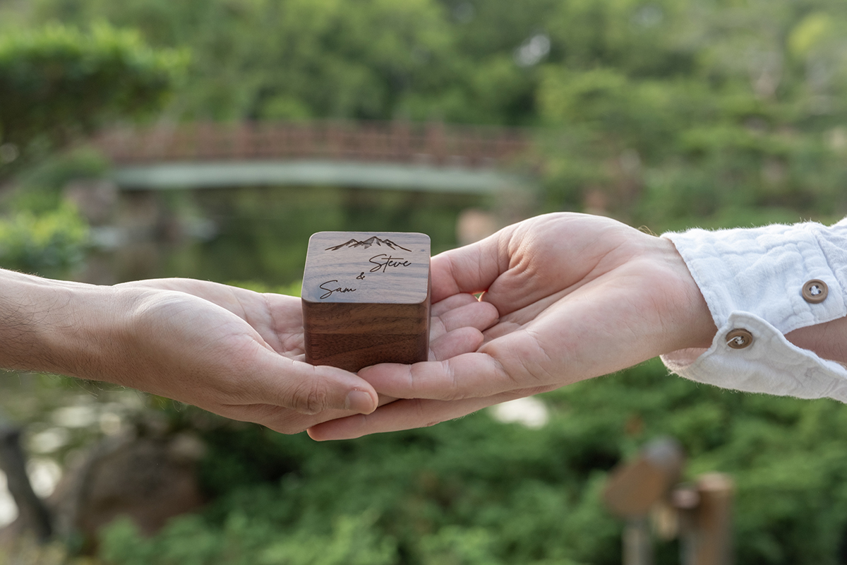 Custom engraved wedding ring box photographed by an LGBTQ+ proposal photographer at Morikami Museum with the Japanese bridge in the background in Delray Beach, Florida.