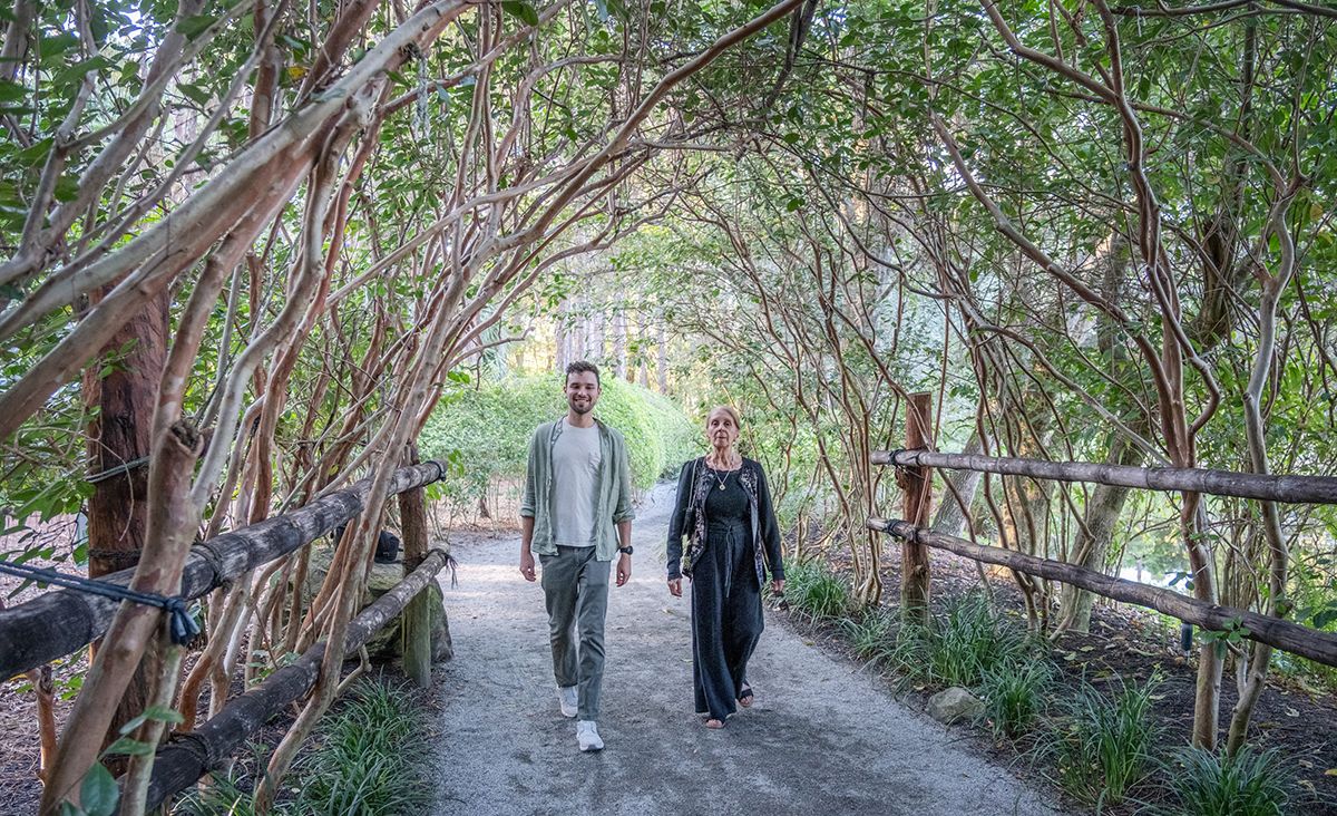LGBTQ+ proposal photographer at Morikami Museum capturing Sam walking with his mother through a natural tree tunnel at Morikami Gardens in Delray Beach, Florida.