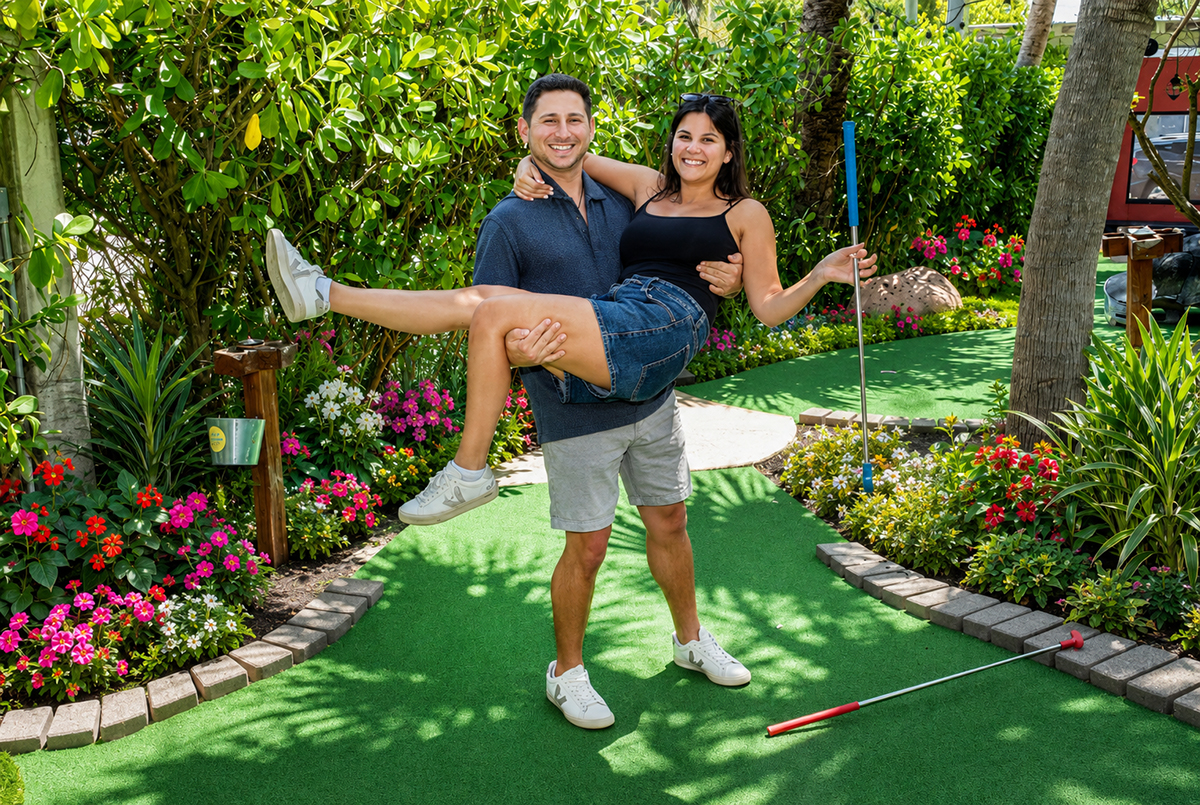 Newly engaged couple celebrates their engagement at Putt’n Around Delray Beach as Jacob lifts Lauren in his arms during a fun mini golf engagement photo session surrounded by tropical landscaping and colorful flowers.