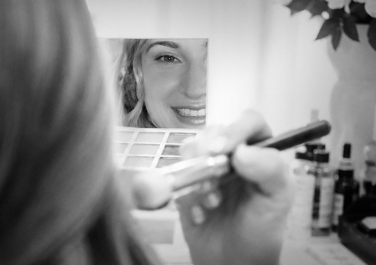 Bride Catarina smiles in a makeup mirror while finishing her wedding preparations before her South Florida Catholic wedding ceremony.