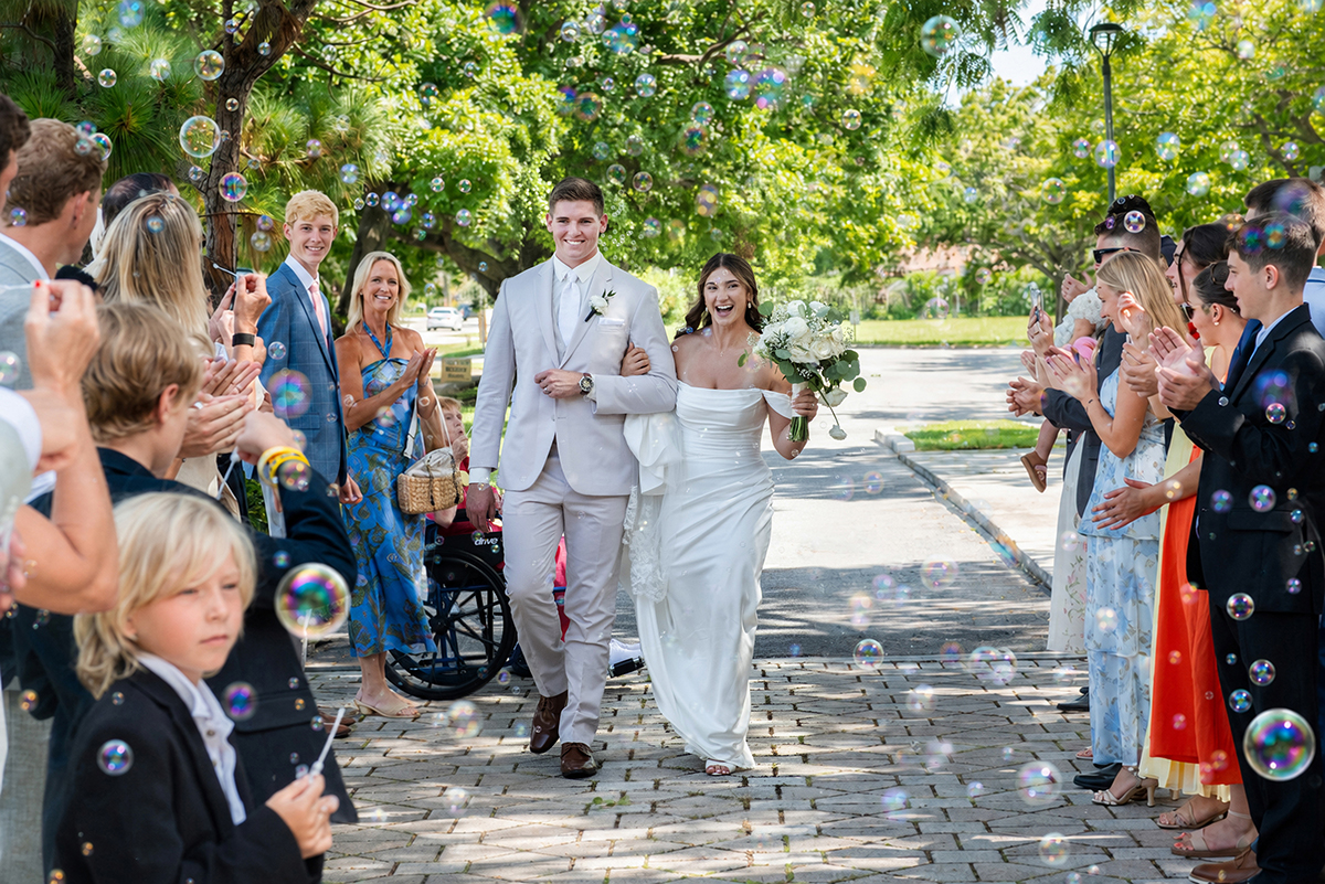 Catarina and David walk through cheering wedding guests and bubbles after their Catholic wedding ceremony at Our Lady of Mercy Catholic Church.