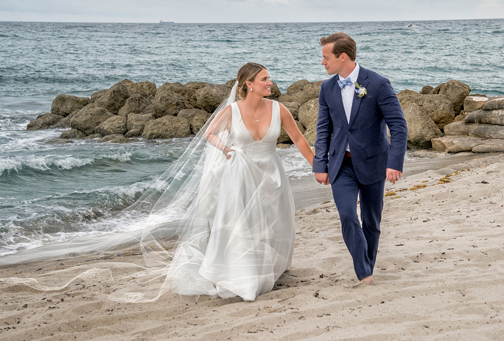 Bride and groom walking along the beach during their luxury wedding at The Boca Raton.