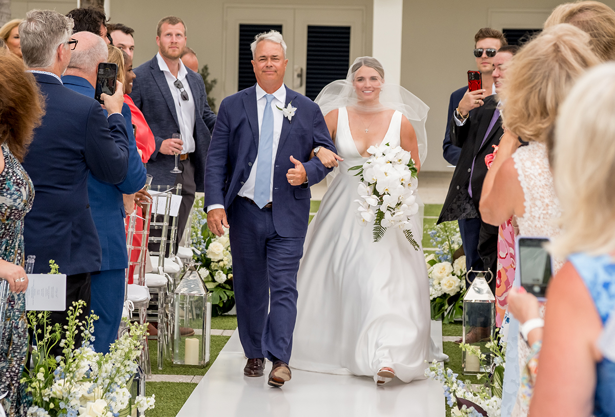 Bride Katie walking down the aisle with her father during her outdoor wedding ceremony at The Boca Raton Beach Club.